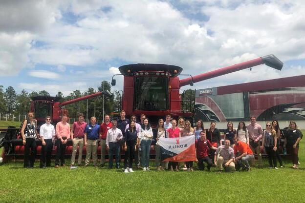 Study abroad students holding an Illinois sign in front of a Case IH tractor