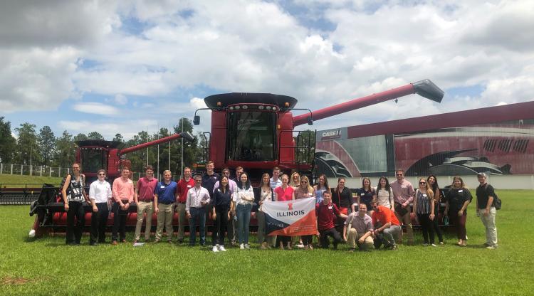 Study abroad students holding an Illinois sign in front of a Case IH tractor