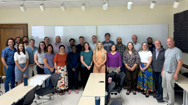 Group of ACE faculty and staff members posing for a photo in front of a white board in a classroom