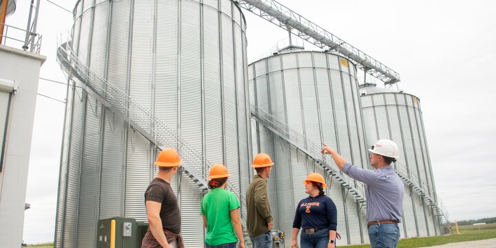 Instructor teaching students in front of grain bins