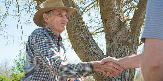 Two people shaking hands in front of a tree