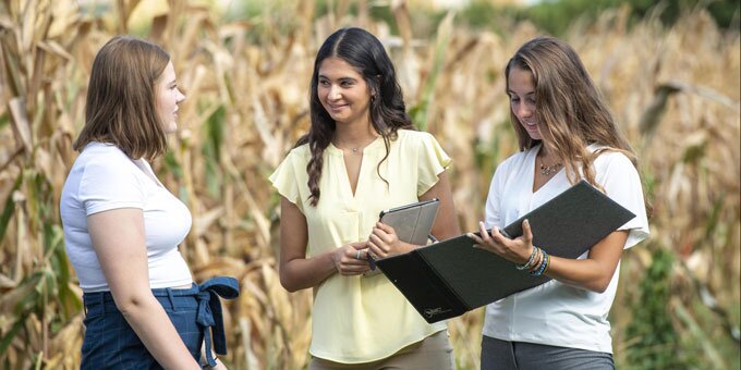 Three students speaking near a corn field