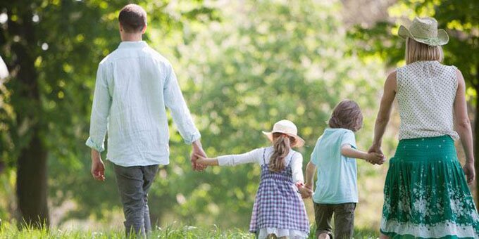 Family of four holding hands and walking through a field