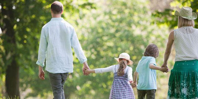Family of four holding hands and walking through a field